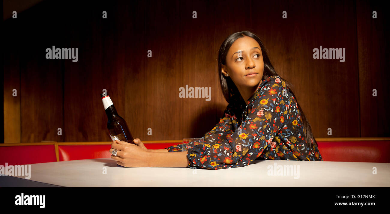 Donna seduta in pannelli di legno azienda stand bottiglia di birra guardando lontano Foto Stock