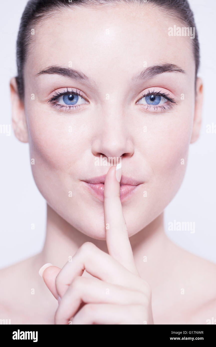 Testa e la spalla colpo di bella giovane donna con il dito sulle labbra Foto Stock