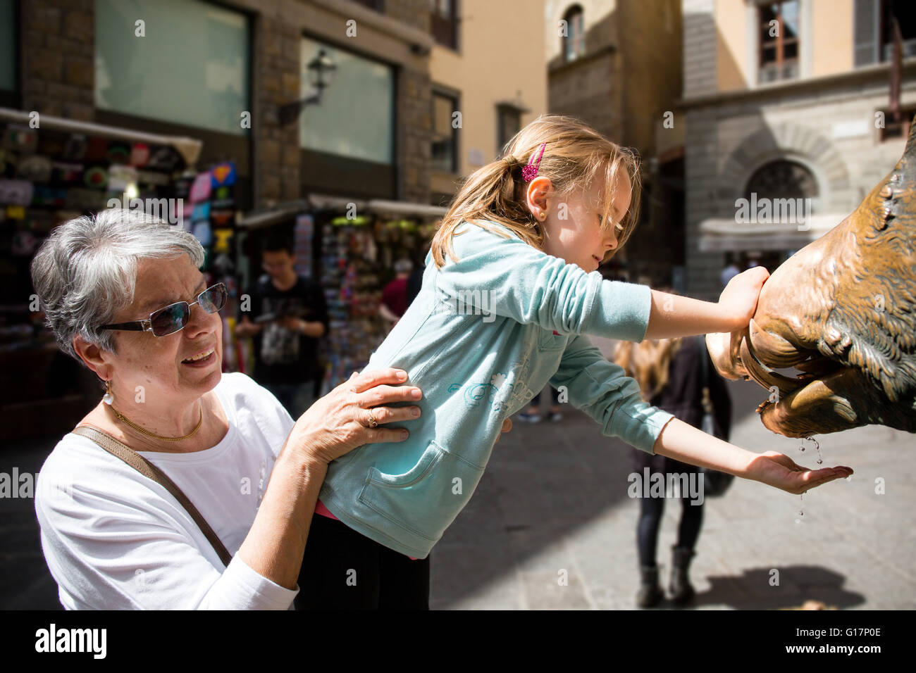Donna Senior e la nipote con la mano sotto l'acqua della fontana, Firenze, Italia Foto Stock