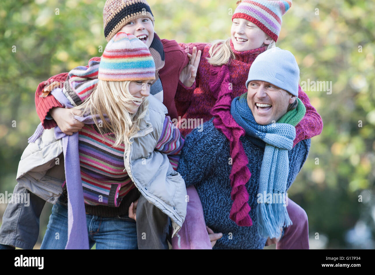 La famiglia insieme nel parco, il padre e la madre il trasporto di bambini sul retro, ridendo Foto Stock