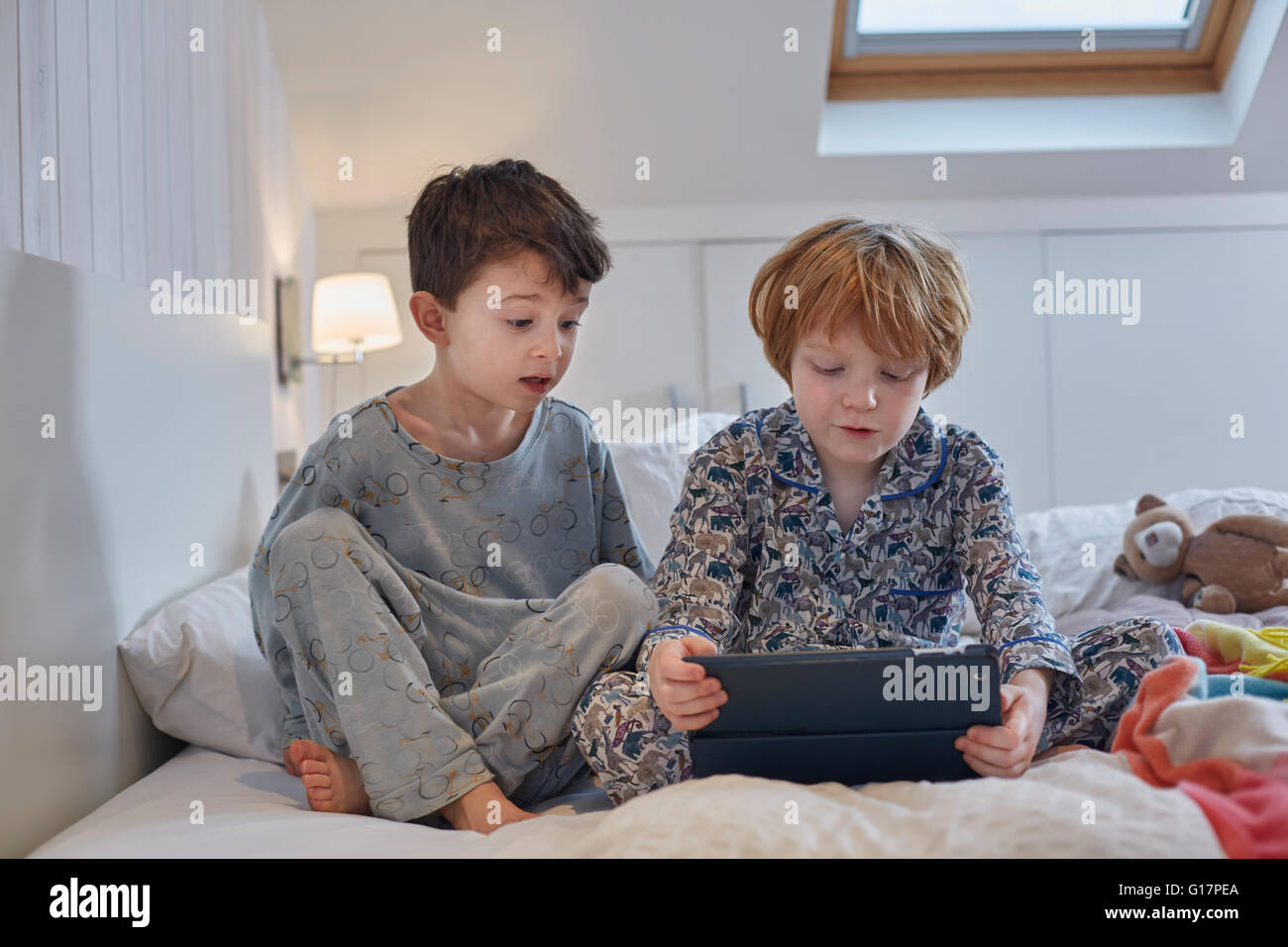 Ragazzi in pigiama con tavoletta digitale a letto Foto Stock