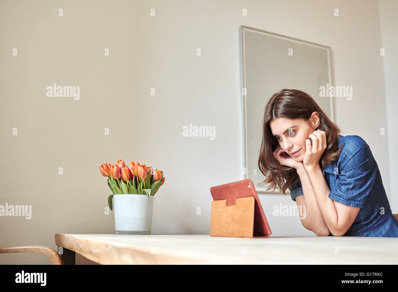 Giovane donna lettura digitale compressa al tavolo da pranzo Foto Stock