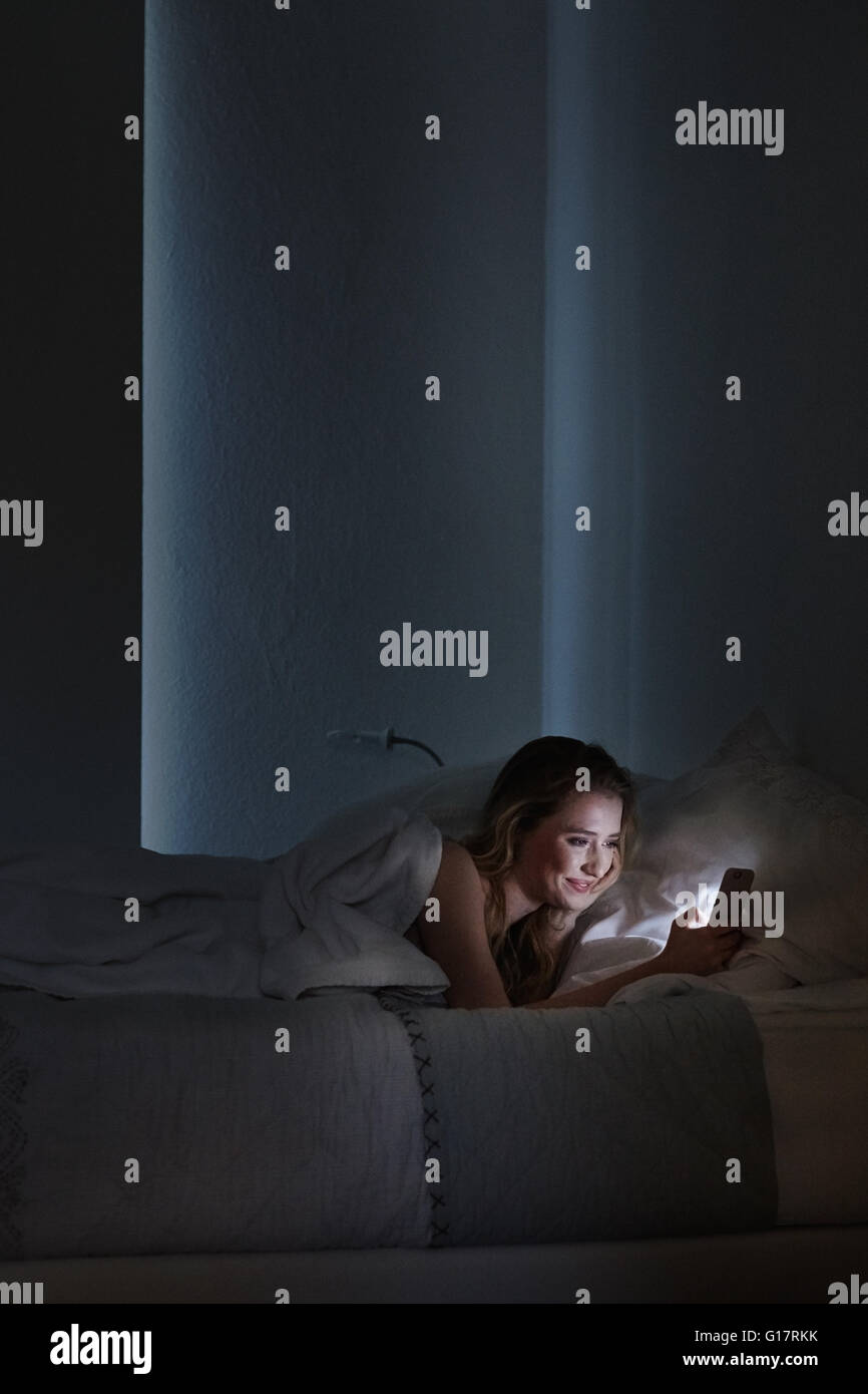 Giovane donna giaceva a letto per la lettura di testi di smartphone di notte Foto Stock