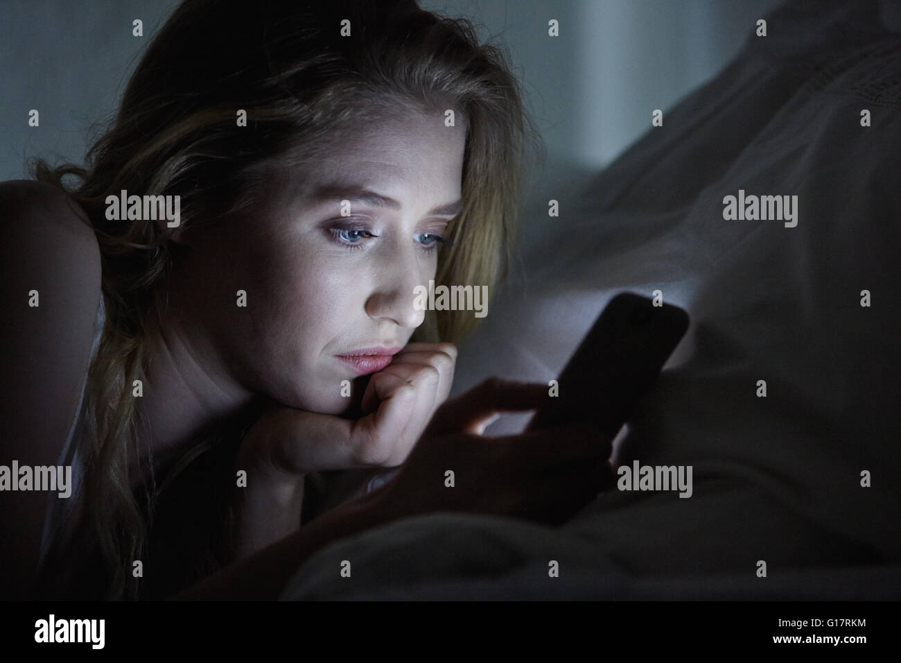 Close up della giovane donna giaceva a letto per la lettura di testi di smartphone di notte Foto Stock