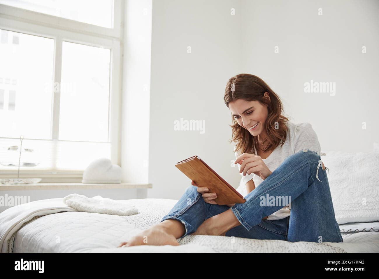 Bella giovane donna seduta sul letto tramite tavoletta digitale Foto Stock