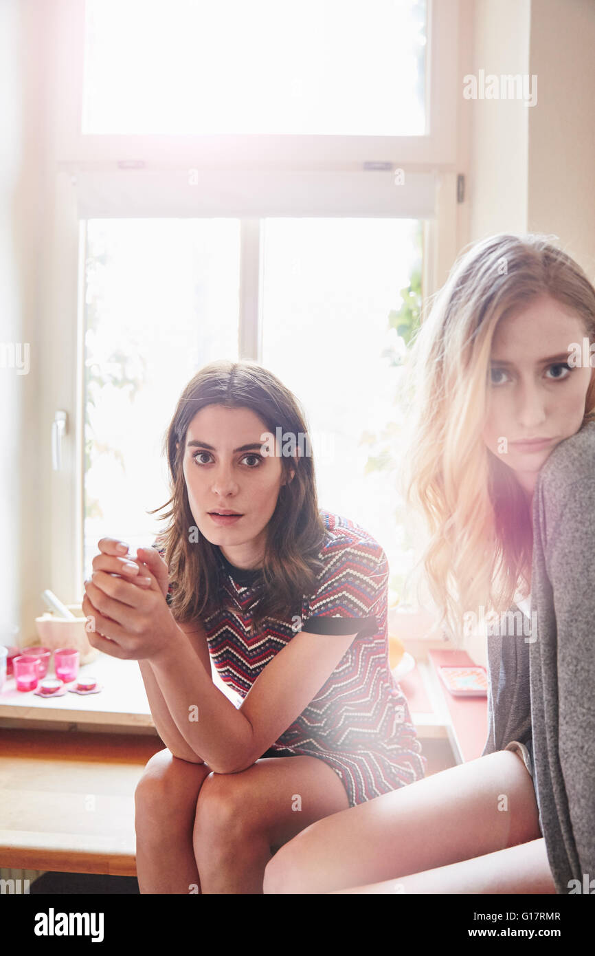 Ritratto di due giovani donne seduta sul banco di cucina Foto Stock