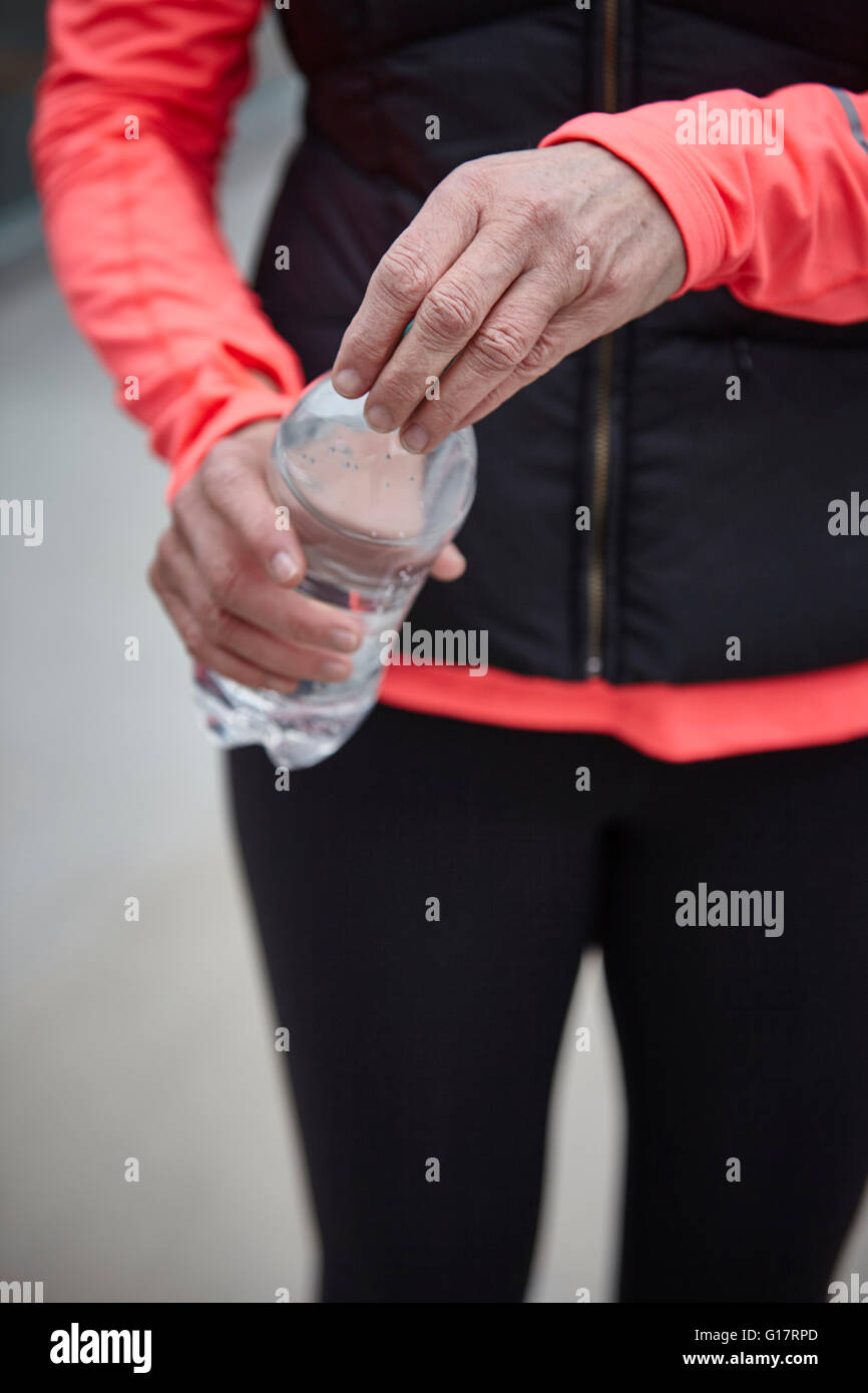 Ritagliato colpo di donna matura formazione, apertura di acqua in bottiglia Foto Stock
