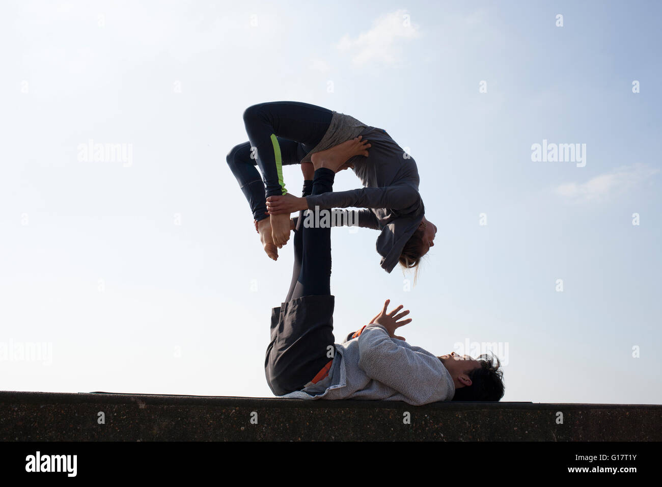 Stagliano l uomo e la donna pratica yoga acrobatico sul muro contro il cielo blu Foto Stock