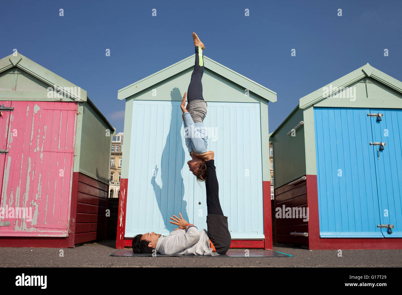 L uomo e la donna pratica yoga acrobatico davanti alla spiaggia di capanne presso la spiaggia di Brighton Foto Stock