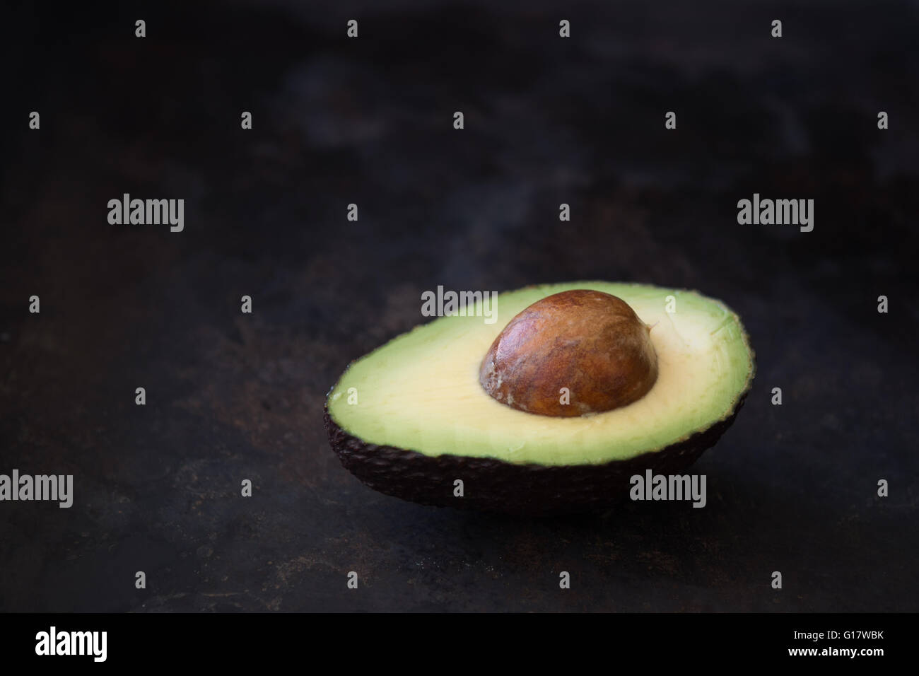 Una metà di un avocado maturo contro un rustico sfondo scuro Foto Stock