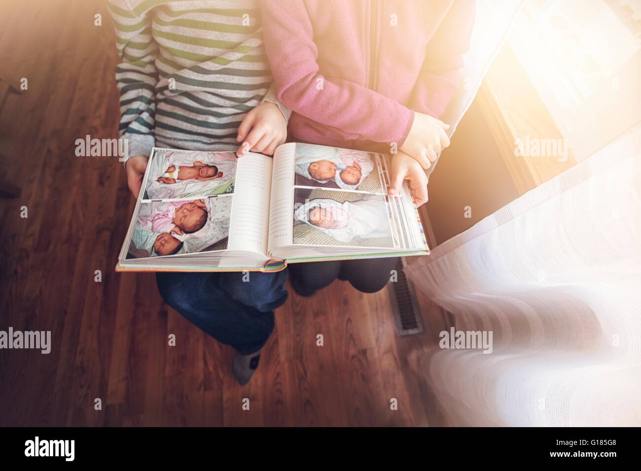 Collo in giù in vista di un ragazzo e una ragazza gemelli guardando album foto di se stessi come i neonati Foto Stock