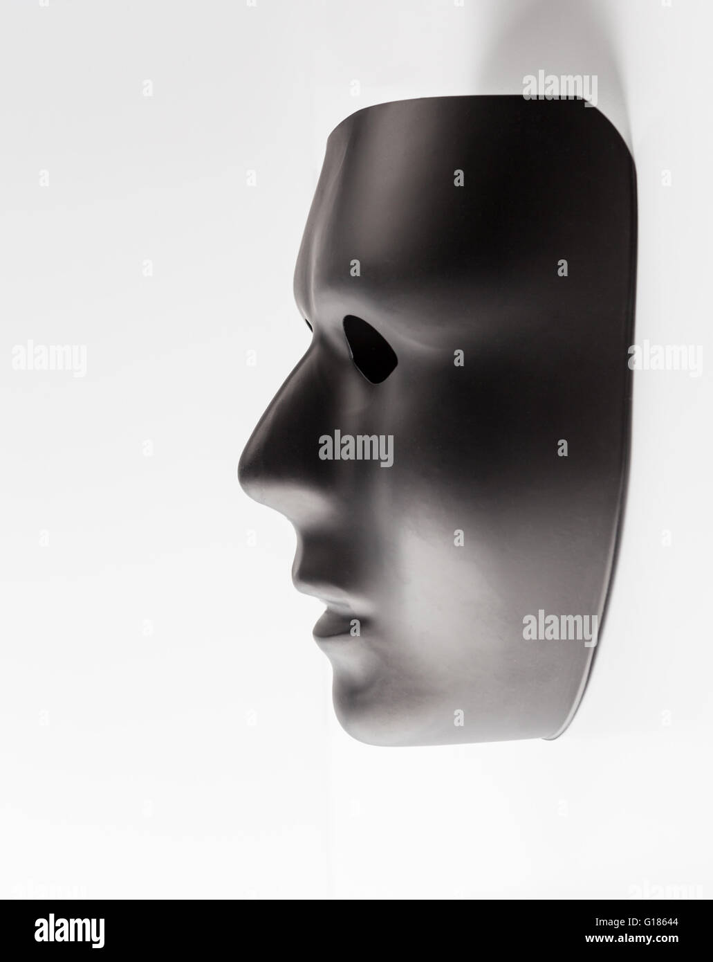 Maschera nera profilo emergente dal fondo bianco. Nascosto il concetto di identità. Foto Stock