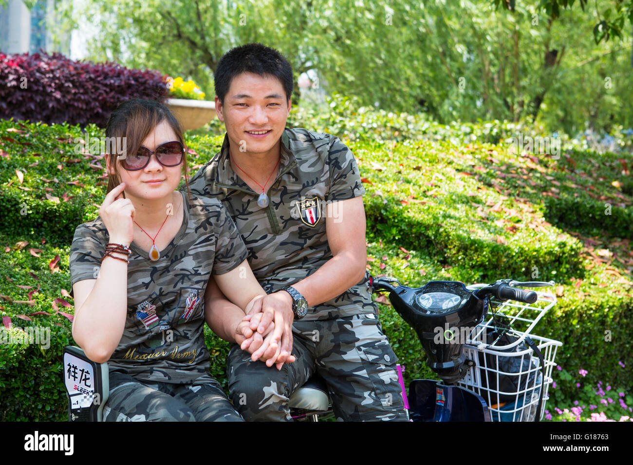 Giovane romantico coppia cinese su uno scooter tenendo le mani nel parco indossando un esercito militare uniforme Foto Stock