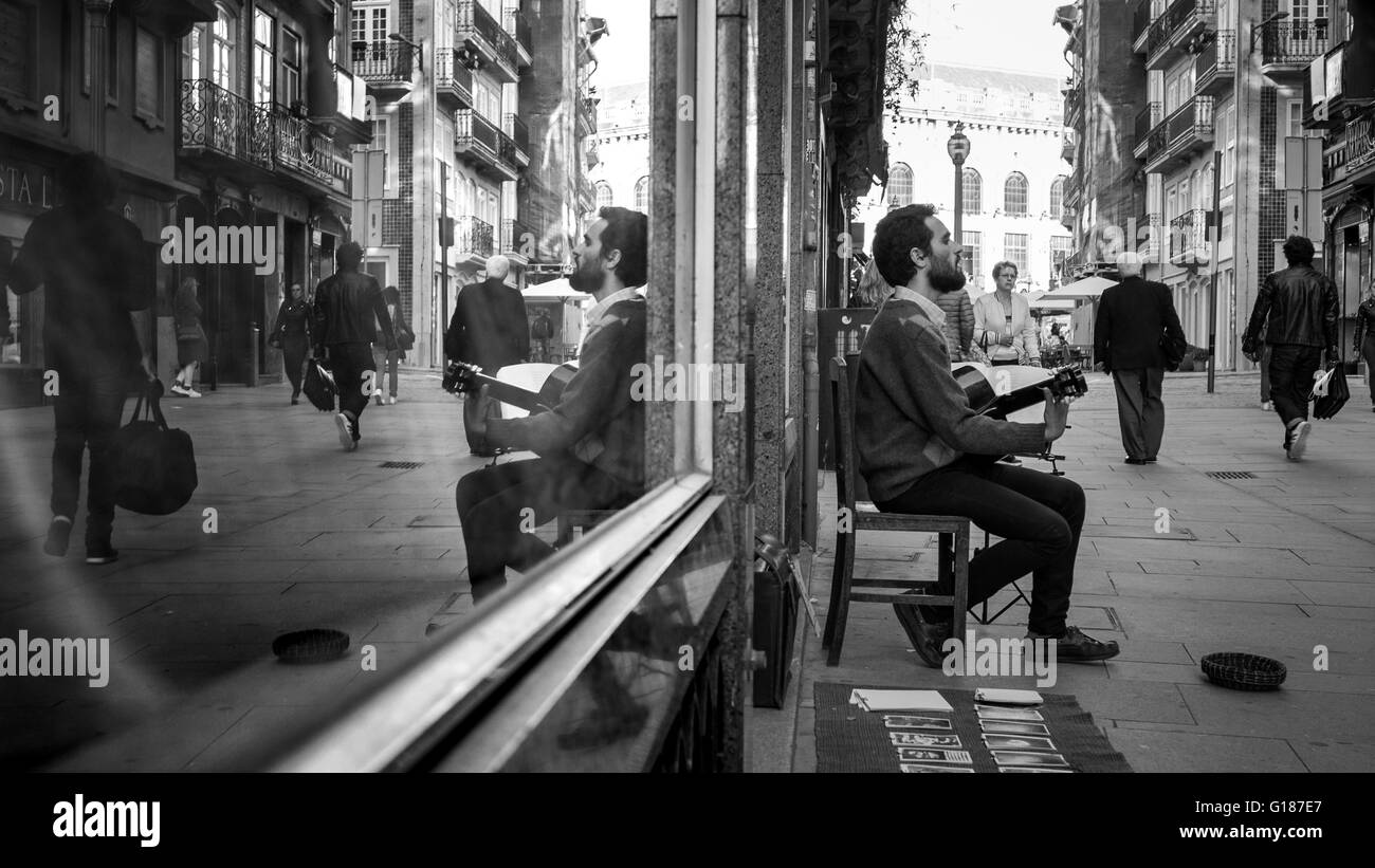 Un maschio di musicista di strada è suonare la chitarra davanti a un negozio di windows, porto, Portogallo. Foto Stock