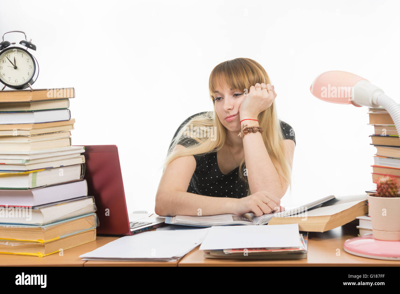Purtroppo lo studente esamina il computer portatile al tavolo tra le pile di libri e giornali Foto Stock