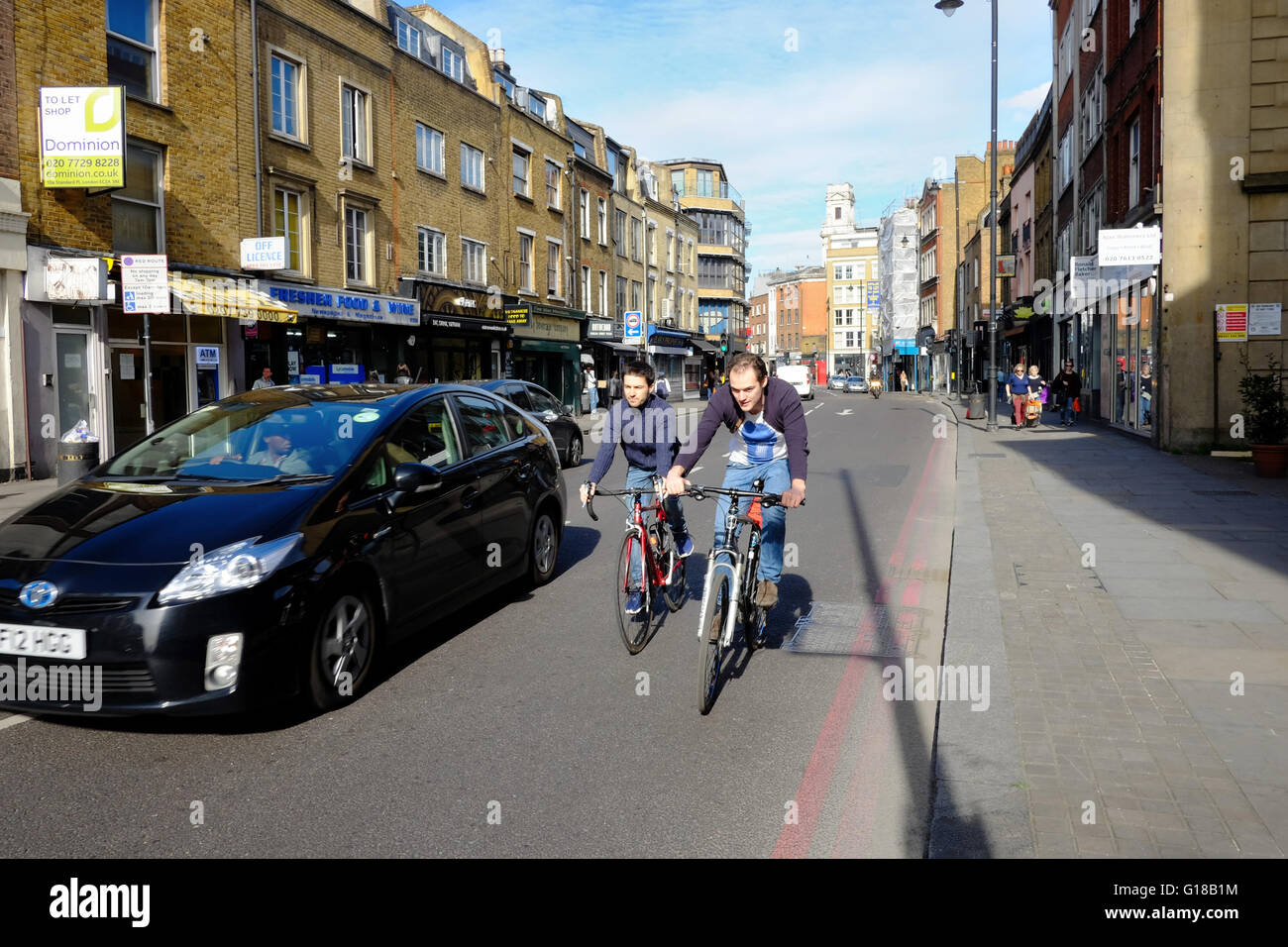 Auto supera due ciclisti in sella a fianco a fianco in Londra Foto Stock