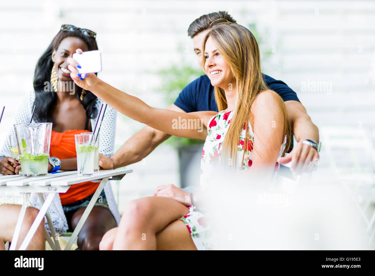 Un gruppo di amici seduti a un tavolo e di parlare di sorridere mentre prendendo selfies in una calda giornata estiva Foto Stock