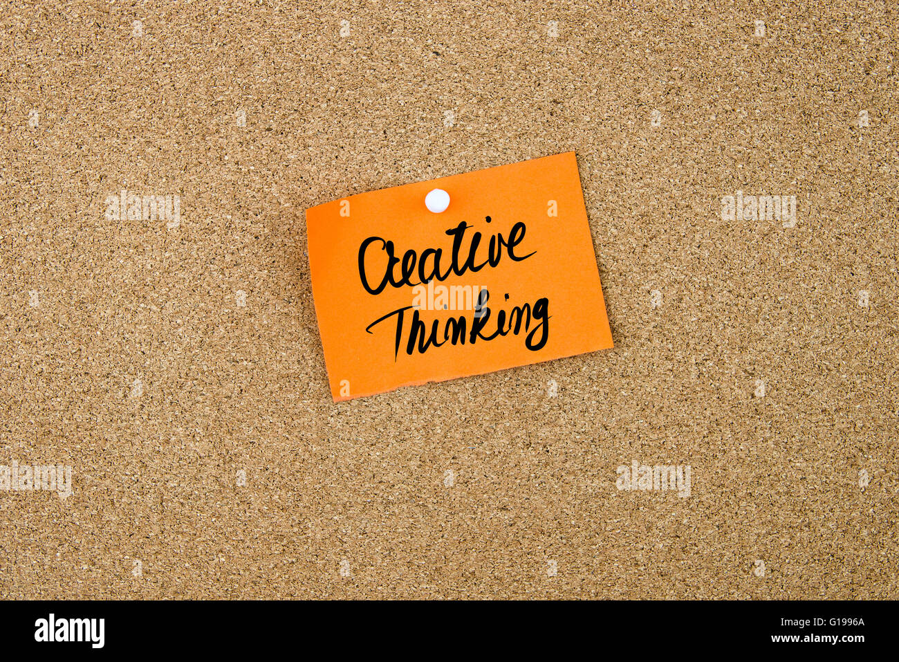 Il Pensiero Creativo scritta sulla carta arancione nota appuntata sulla bacheca di sughero con il bianco thumbtacks, copia dello spazio disponibile Foto Stock