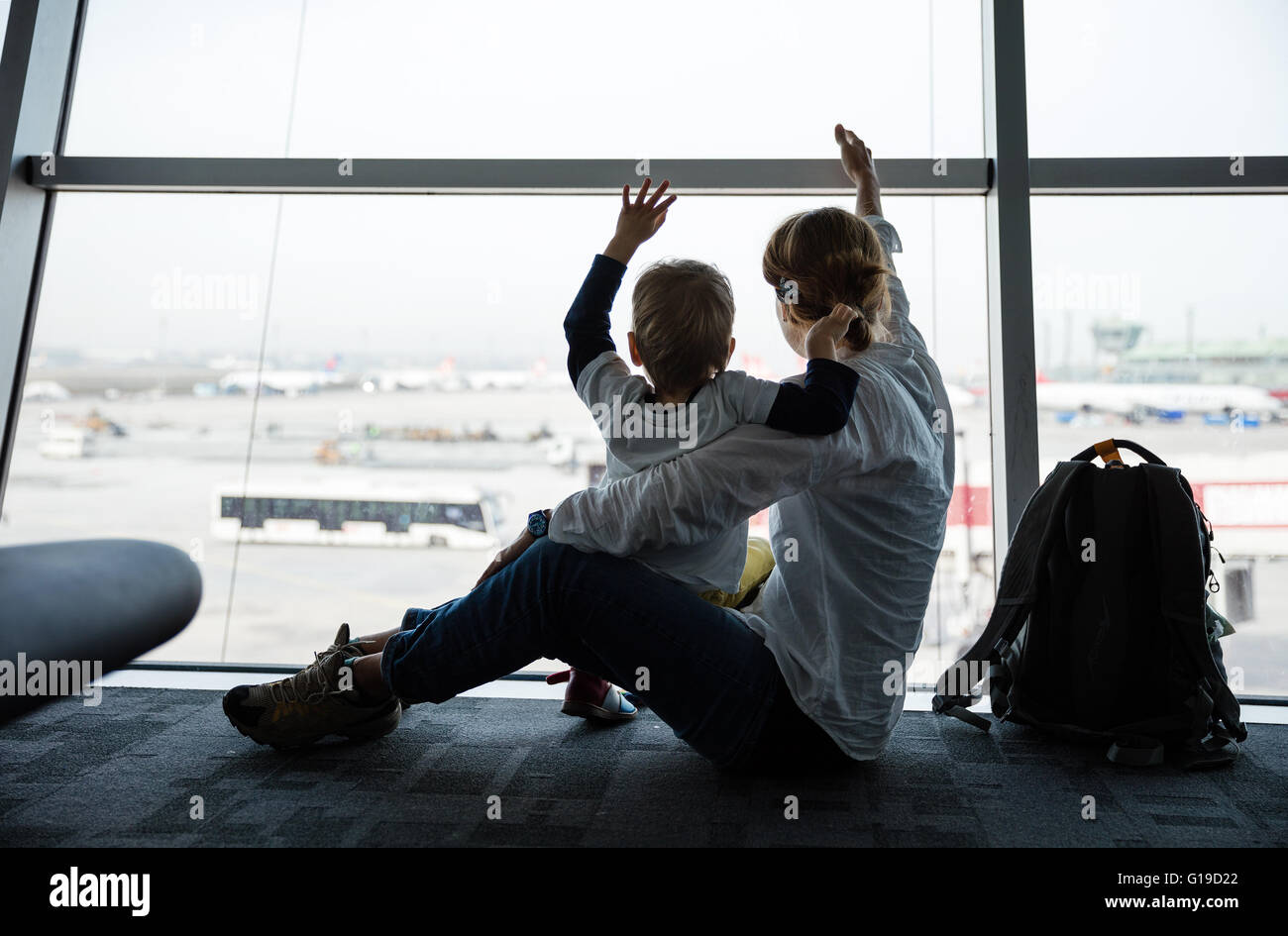 Madre e figlio seduti vicino al finestrino in aeroporto e agitando le mani per aerei Foto Stock