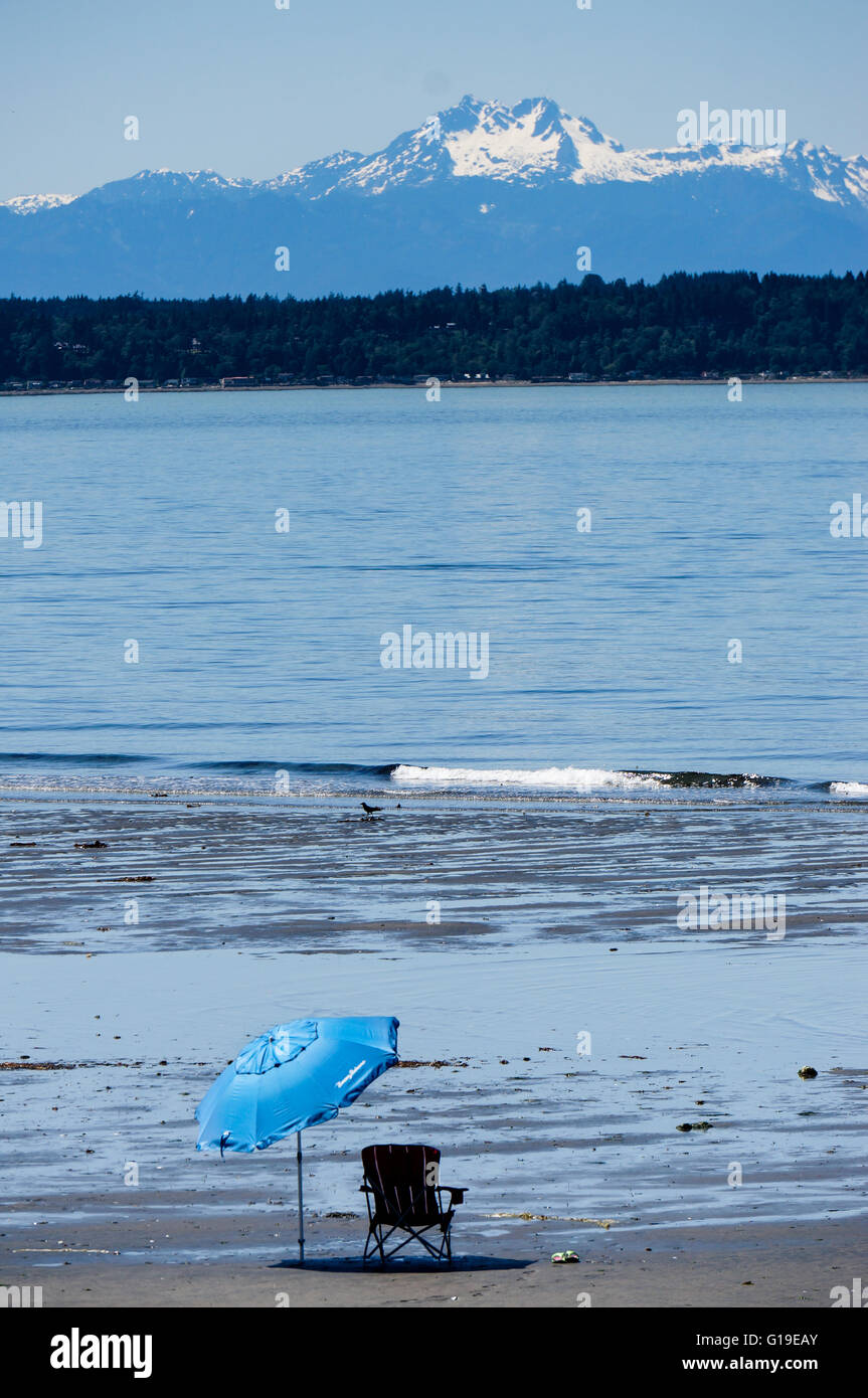 Sedia e ombrello blu sulla sabbia a bassa marea sul Puget Sound con la snowy Olympic Mountain Range e Bainbridge Island in backgr Foto Stock