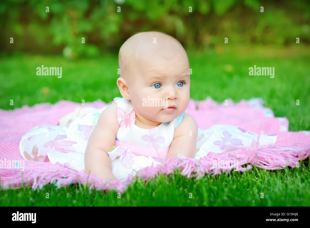 Baby sorridente e cercando fino alla fotocamera all'aperto alla luce diretta del sole Foto Stock