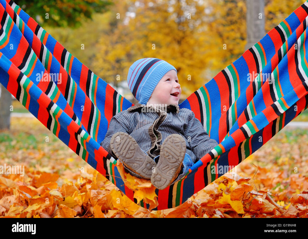 Gioiosa baby boy in autunno parco su una amaca Foto Stock