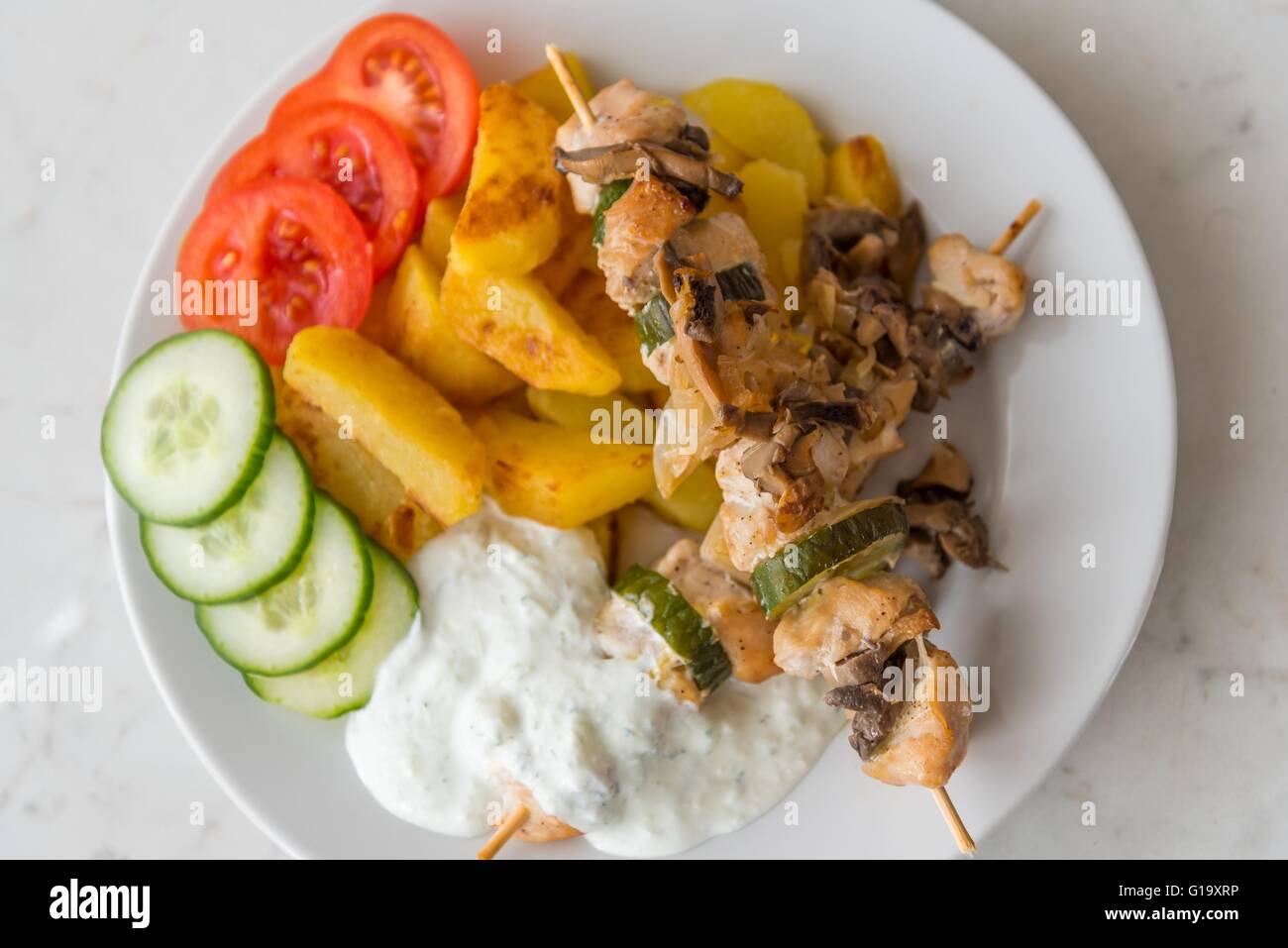Tradizionale delizioso pollo shish kebab con funghi. Servito con patate americane, cetriolo, pomodoro e tzatziki medicazione Foto Stock