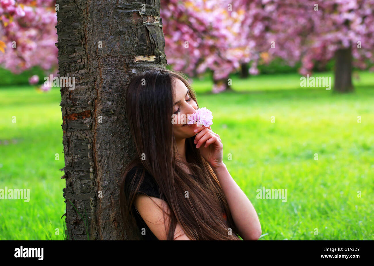 Felice bella giovane donna in fiore parco con alberi e fiori. Foto Stock