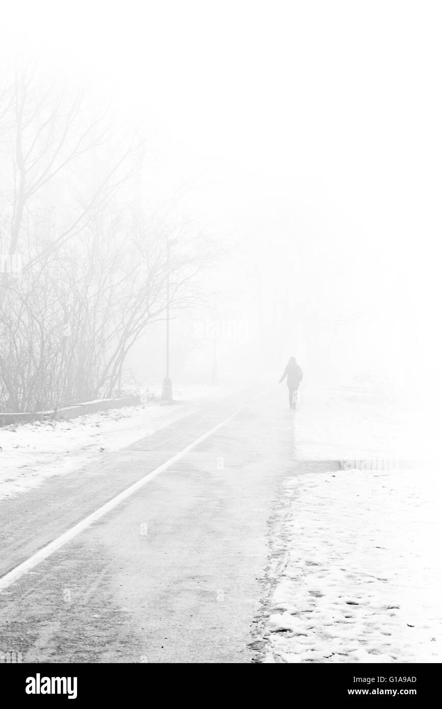 La donna a piedi lungo una strada in una nebbiosa mattina di neve Foto Stock