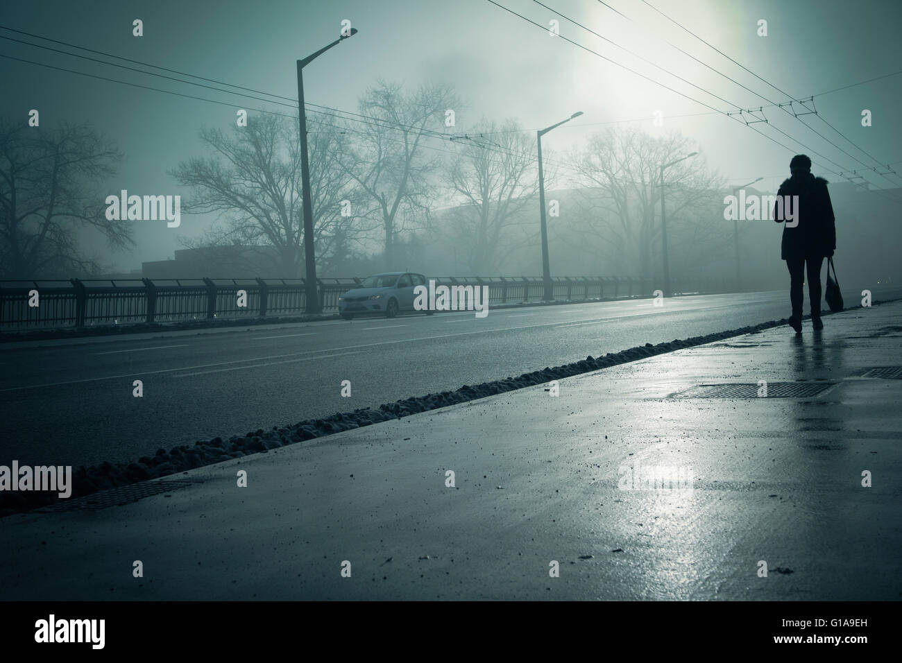 Silhouette di una donna che cammina lungo un tratto di strada Foto Stock