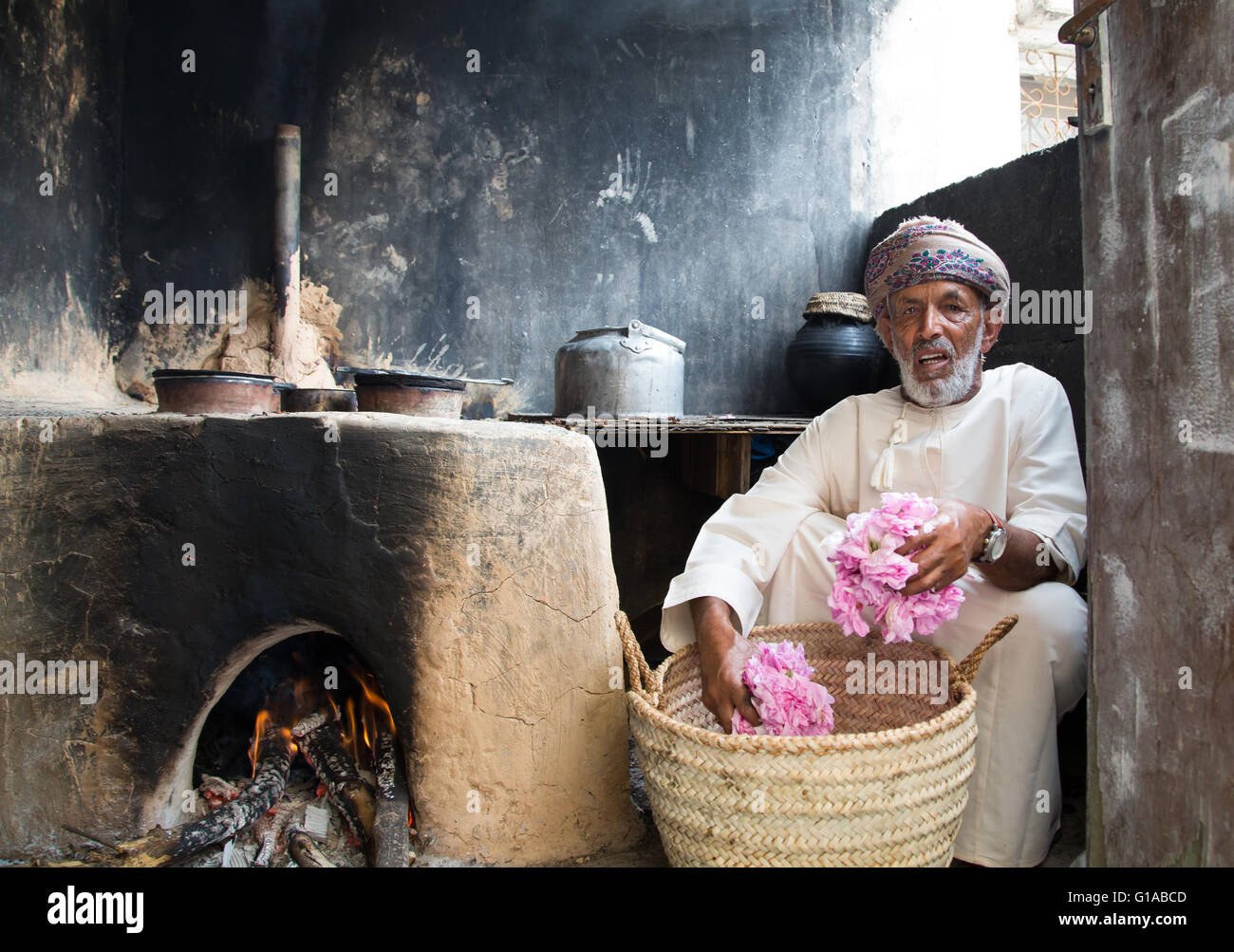 Il vecchio uomo Omani con benna piena di petali di rosa davanti a un forno utilizzato per la realizzazione di rosewater Foto Stock