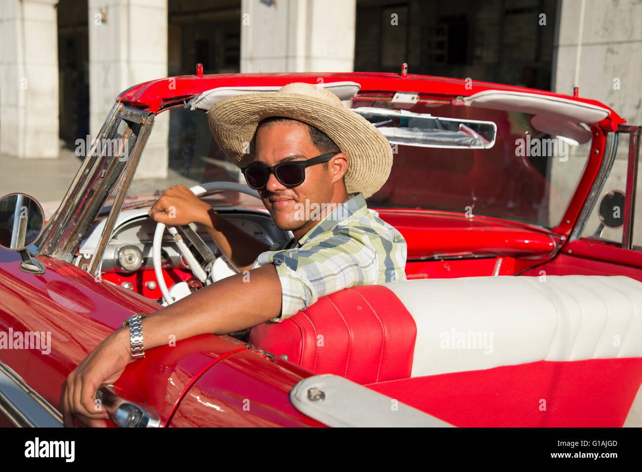 Giovane uomo cubano indossando un cappello da cowboy e occhiali da sole si siede nel sedile di guida di una anni cinquanta ci rosso classico auto in Havana Cuba Foto Stock