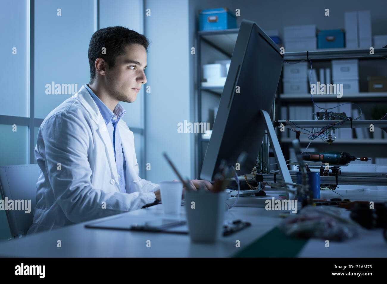 Fiducioso studente di ingegneria lavorando nel laboratorio e utilizzando un computer, stampante 3D in background, tecnologia e innov Foto Stock