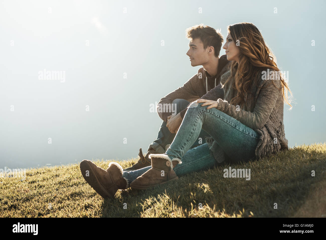 Sorridente coppia giovane seduto sull'erba durante una giornata di sole, guardando lontano e sognare il loro futuro Foto Stock