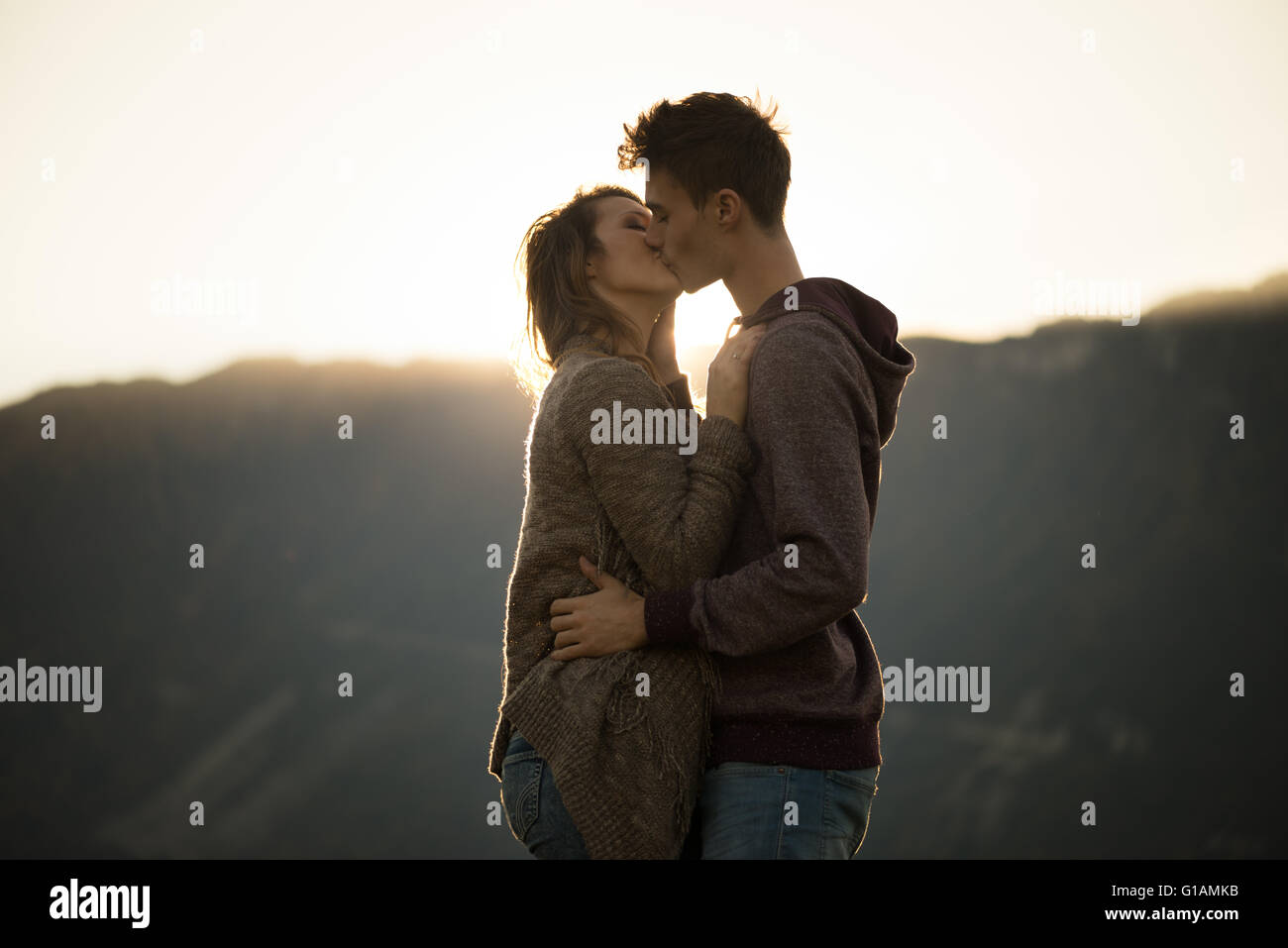 Romantico coppia giovane bacia appassionatamente al tramonto, montagne sullo sfondo, i sentimenti e le relazioni di concetto Foto Stock