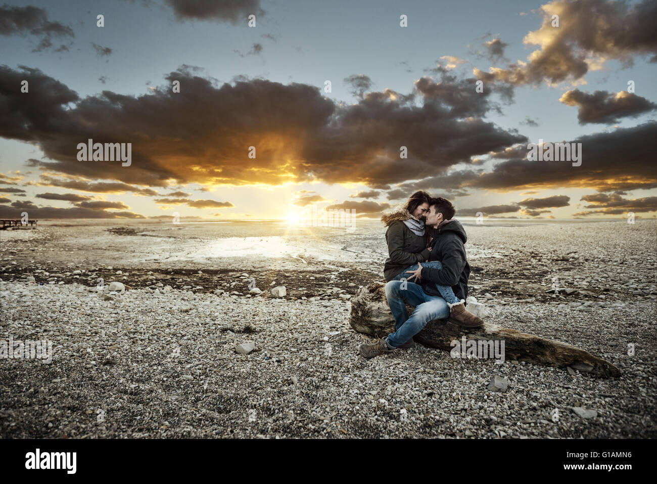 Coppia giovane avente una data romantica al lago, stanno abbracciando e seduta su un tronco sulla spiaggia, di amore e di relazioni di co Foto Stock