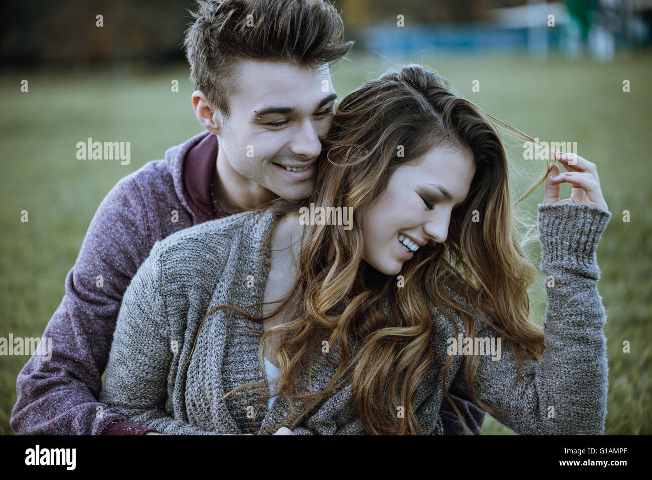 Giocoso coppia giovane seduto sull'erba e abbracciando, stanno ridendo e godendo Foto Stock