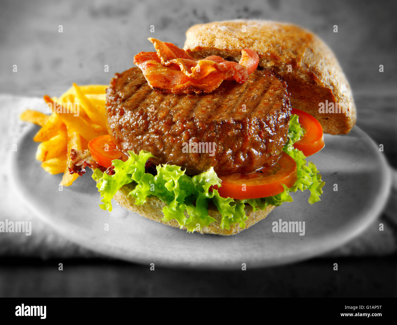 Hamburger di manzo con la pancetta in un panino integrale con insalata e patatine fritte Foto Stock