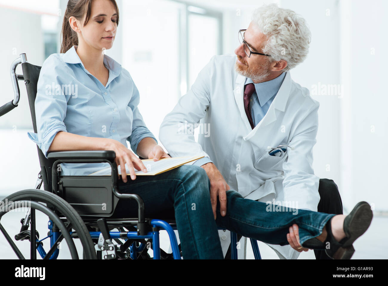 Medico di visitare una donna non valido in carrozzella, egli sta esaminando la sua gamba, riabilitazione e concetto physioteraphy Foto Stock
