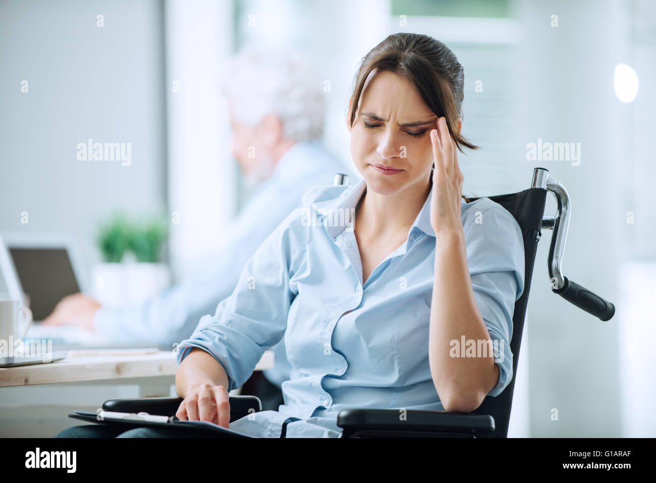 Disabili business donna in carrozzella a ufficio avente un mal di testa di toccare i suoi templi Foto Stock