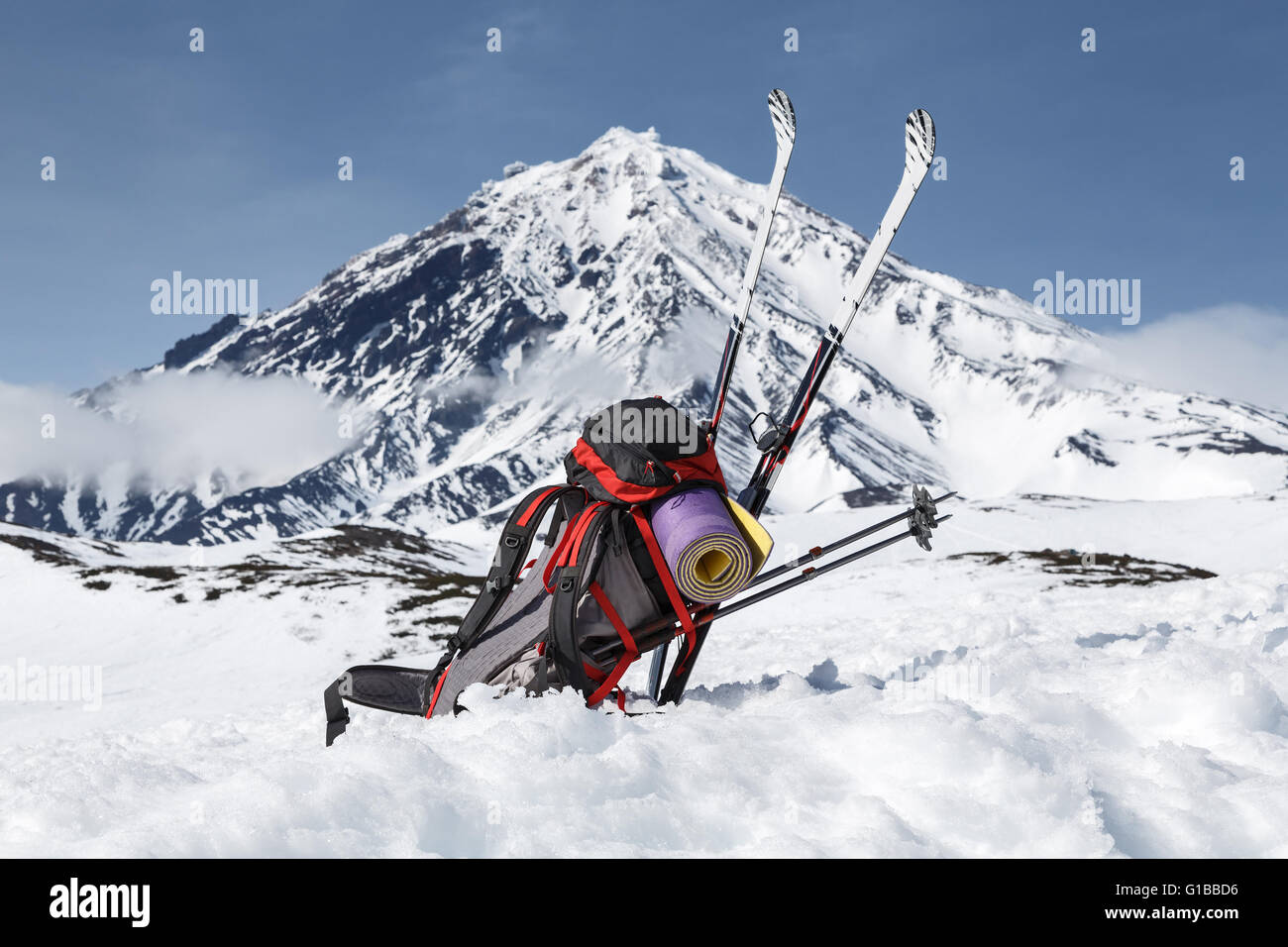 Zaino, sci e le racchette giacciono sulla neve sul vulcano di sfondo Foto Stock