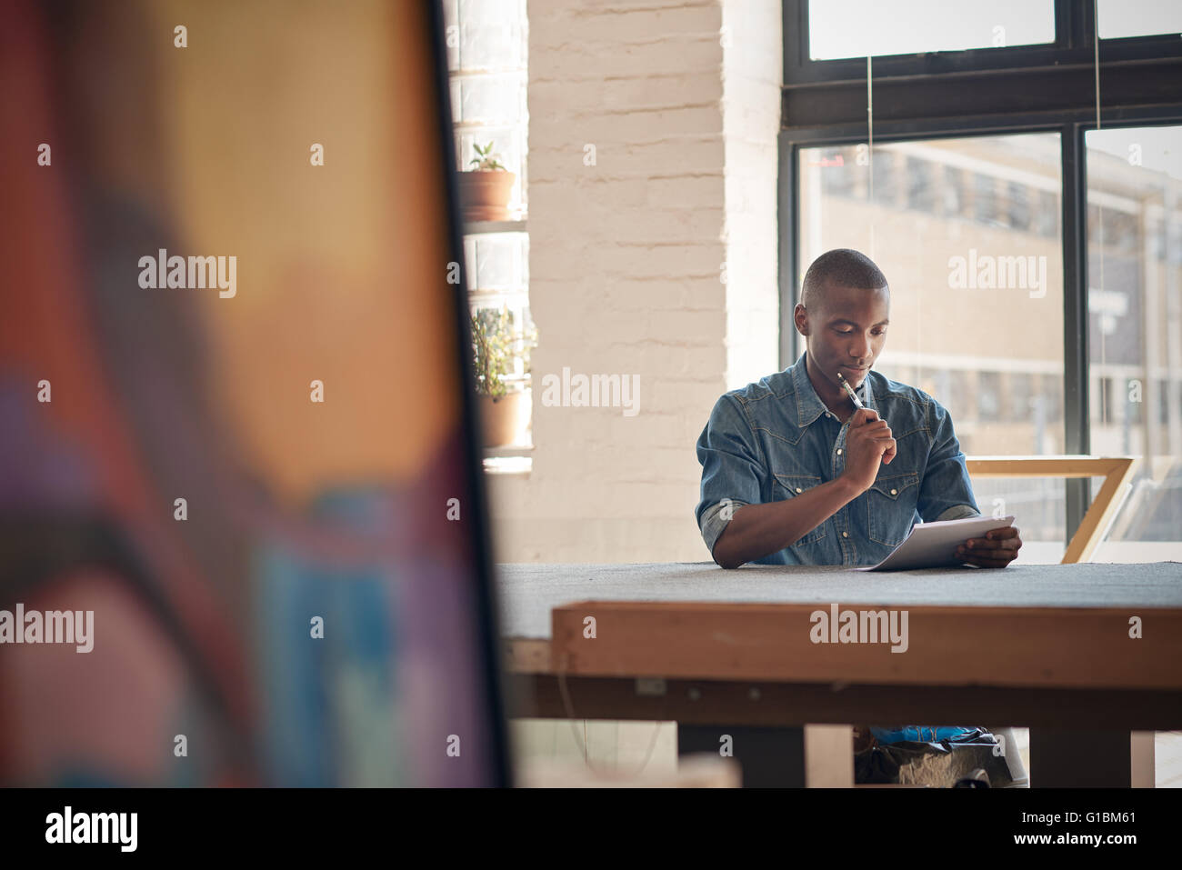 Bel giovane imprenditore Afican seduti ad un tavolo di lavoro con carta e penna, soffermandosi a pensare mentre facendo piani per il suo futuro Foto Stock