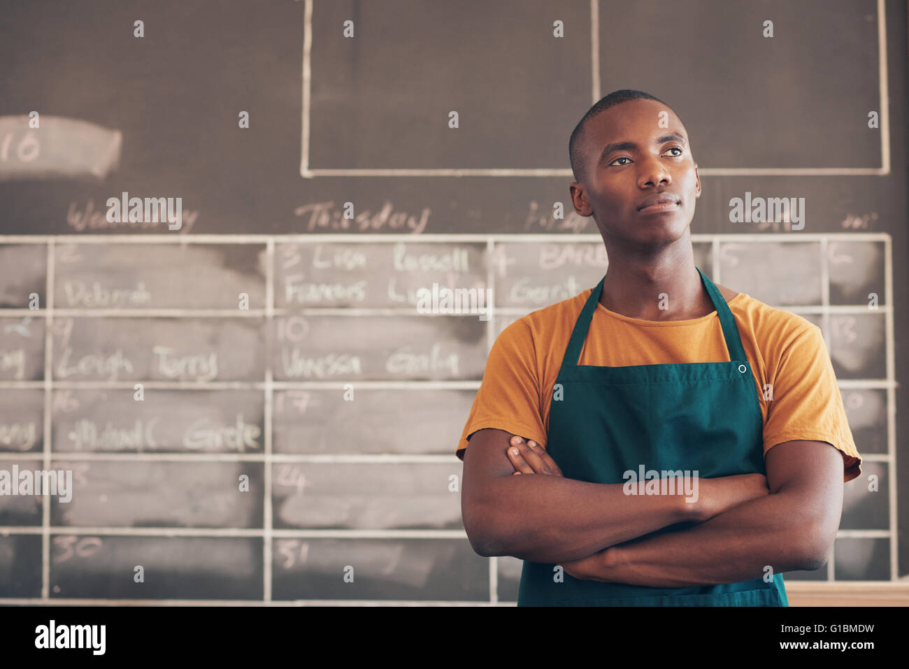 Bel giovane artigiano della discesa africana in piedi con le braccia piegate e indossare un grembiule, pensando al suo entrepreneuri Foto Stock