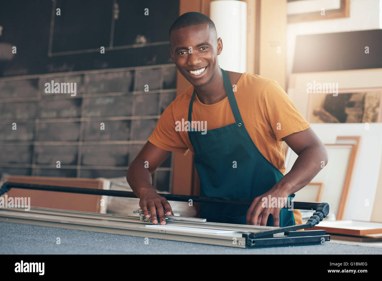 Ritratto di un giovane africano artigiano mettendo in pausa per dare la fotocamera con un bel sorriso, mentre si lavora con abilità utilizzando un utensile di taglio Foto Stock