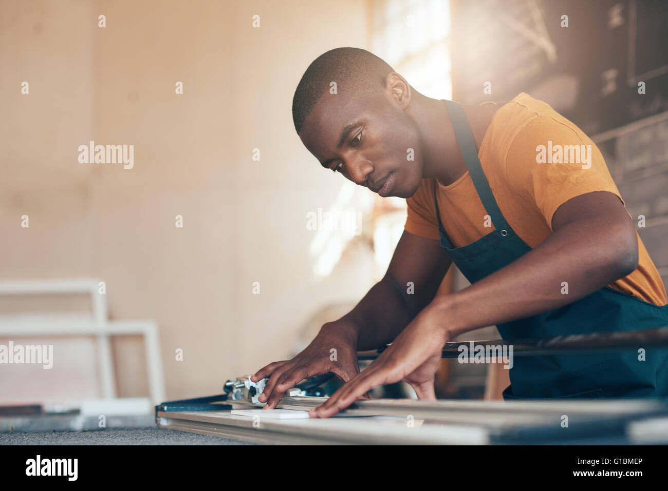 Giovane artigiano della discesa africana concentrandosi attentamente mentre utilizzando un utensile di taglio con abilità e competenze in un splendidamente Foto Stock