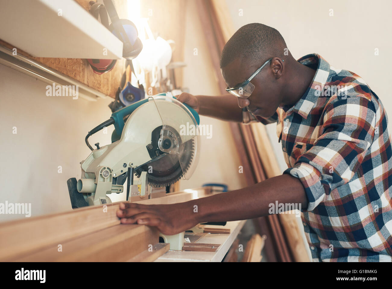 Giovani aritsan della discesa africana lavora con esperienza in un laboratorio di falegnameria, gestione di una sega circolare, e indossano la sicurezza g Foto Stock