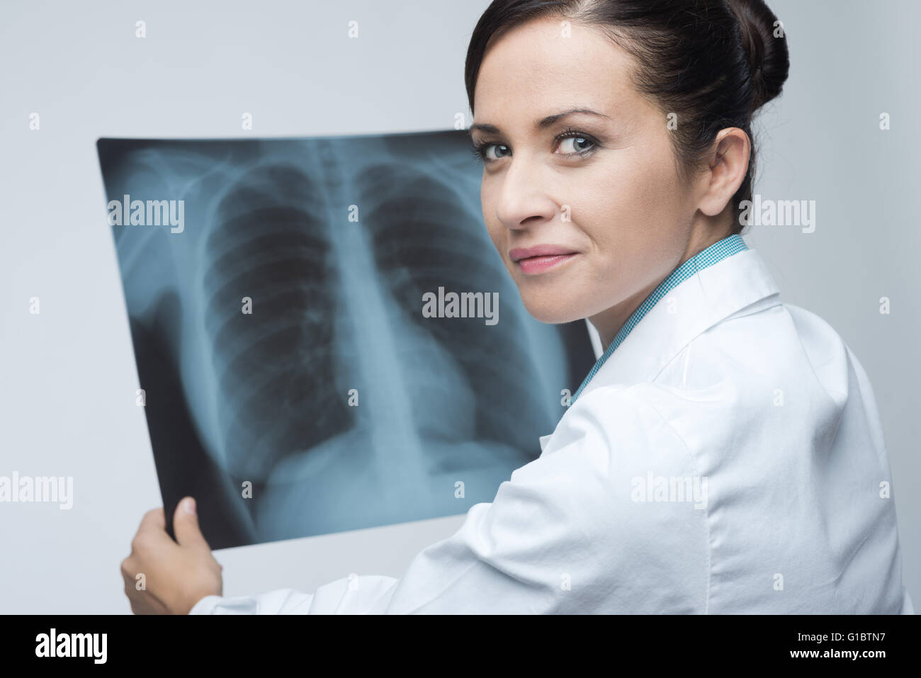 Sorridente attraente medico donna il controllo di una gabbia costale immagine a raggi x. Foto Stock