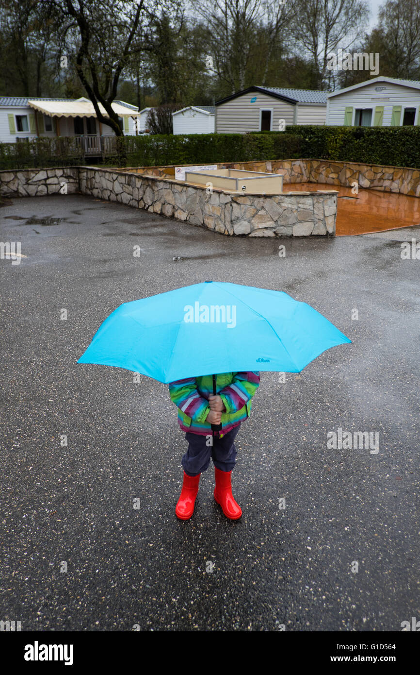 Bambino con wellies e ombrello sotto la pioggia su un campeggio in aprile, Francia Foto Stock