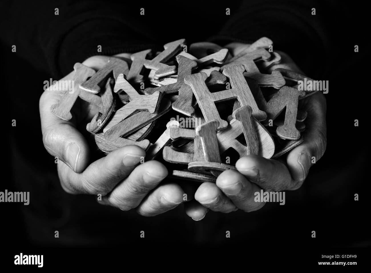 Primo piano delle mani di un giovane uomo con una manciata di diverse lettere di legno, contro uno sfondo nero, in nero e di Pentecoste Foto Stock
