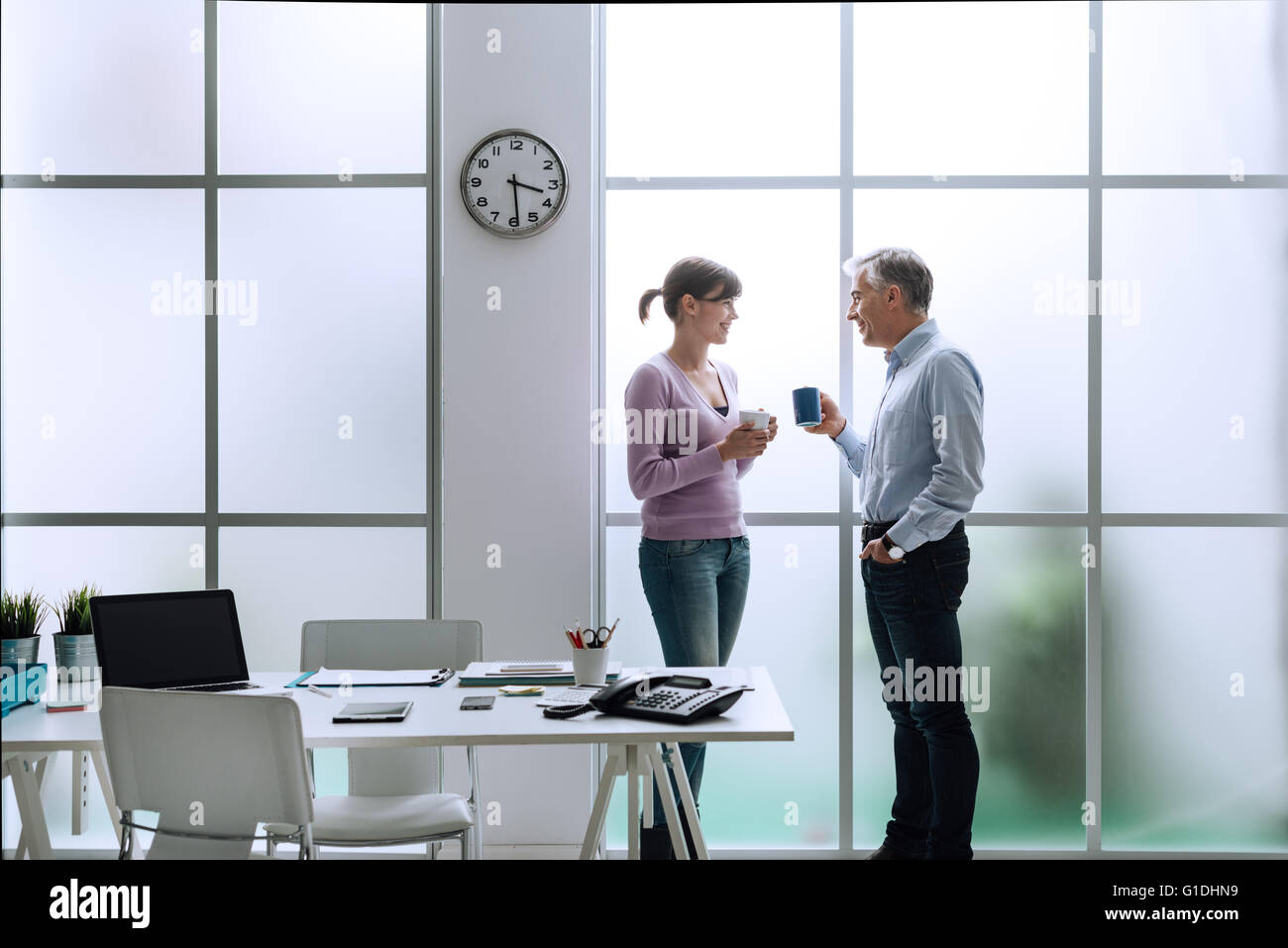 Allegro impiegati in ufficio, rilassante, avente una pausa caffè e chiacchierare insieme, essi sono in piedi nella parte anteriore del Foto Stock